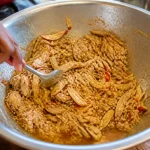 Main mélangeant chiquetaille de poulet effiloché dans un grand bol métallique